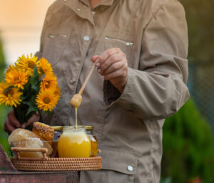 What Beekeepers know that most shoppers do not. Someone dipping stick into honey jar with flowers and official top on